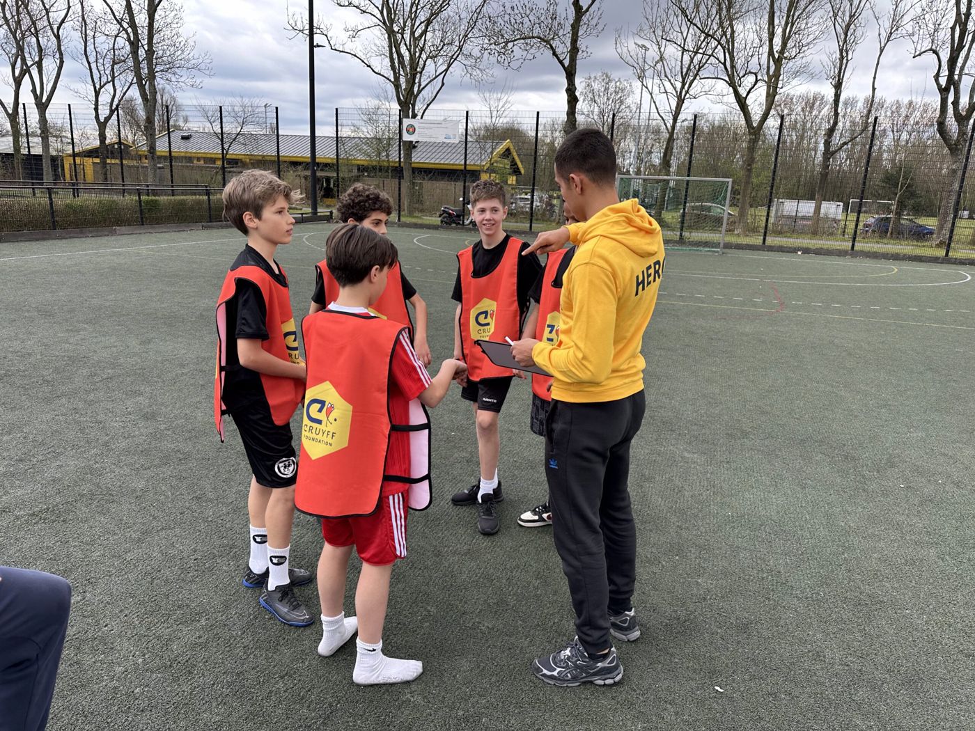 Coach geeft uitleg aan een groep kinderen op een voetbalveld